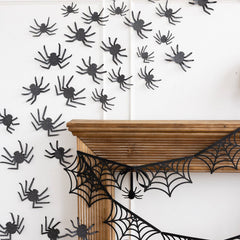 Halloween decorations with black spiders and webs on a white wall.