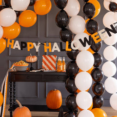 Halloween-themed room with balloon arch, pumpkins, and 'Happy Halloween' banner.